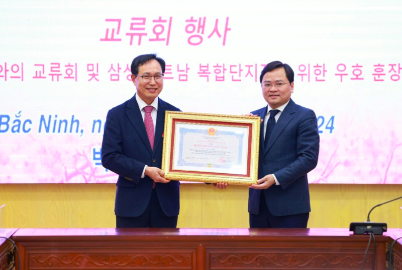 Secretary of the Bac Ninh Provincial Party Committee Nguyen Anh Tuan (right), authorized by the State President, presents General Director of Samsung Vietnam Choi Joo Ho with a friendship insignia.